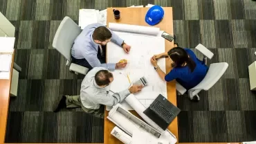 Tres personas revisan planos en una sala de reuniones.